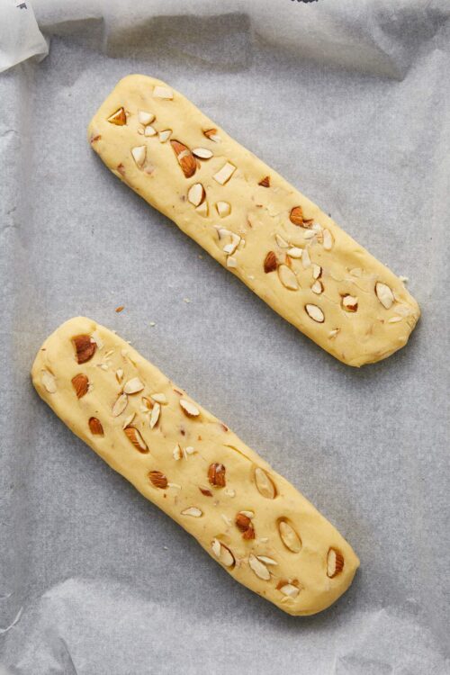 Buttery almond biscotti dough with sliced almonds before baking on parchment paper.