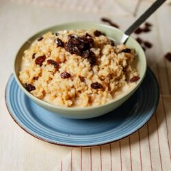 Creamy rice pudding with raisins served in a bowl on a wooden table.