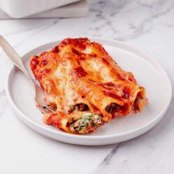Baked cheese and spinach cannelloni on a white plate with a marble background.