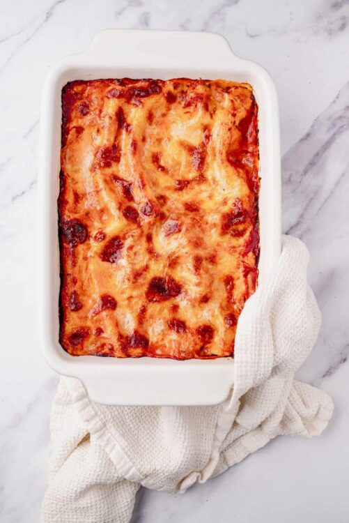 Golden baked lasagna in a white baking dish on marble countertop.