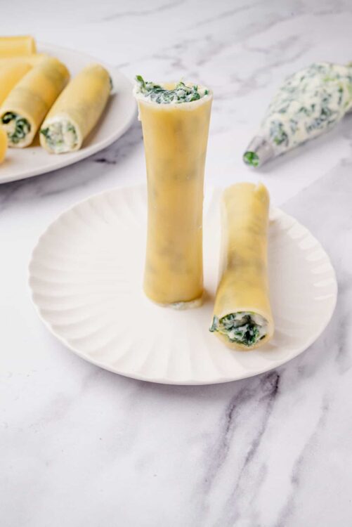 Silky spinach and cheese cannelloni on a white plate topped with creamy sauce.