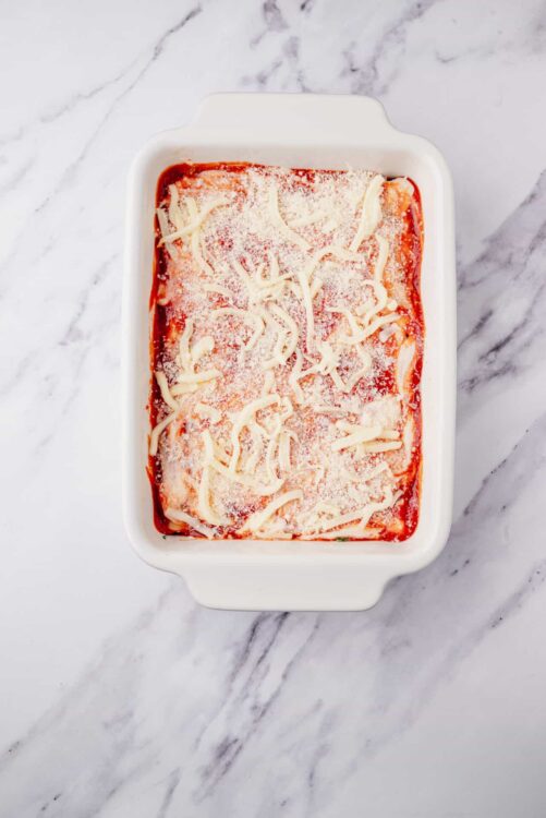 Cheese and marinara baked ziti in a white casserole dish topped with shredded cheese, ready to bake or serve.