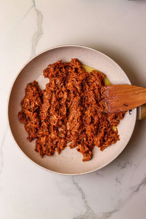 Slow cooker shredded beef in a beige skillet for savory recipes.