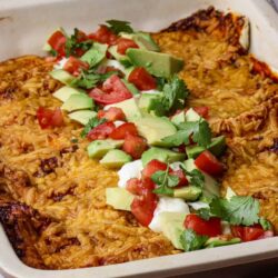 Cheesy chicken and rice casserole with fresh avocado and tomato garnish in a baking dish.