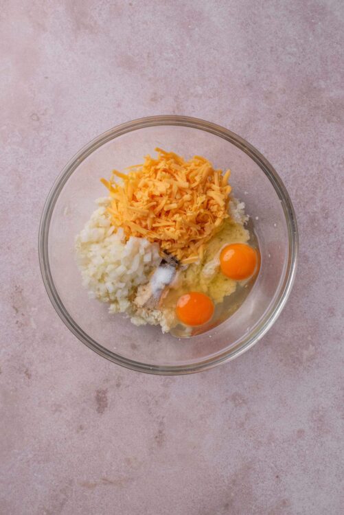 Cream cheese mixture with shredded cheddar, diced onions, eggs on beige background.