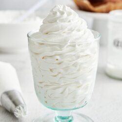 Fluffy whipped cream in a clear glass dessert cup, perfect for desserts or topping.