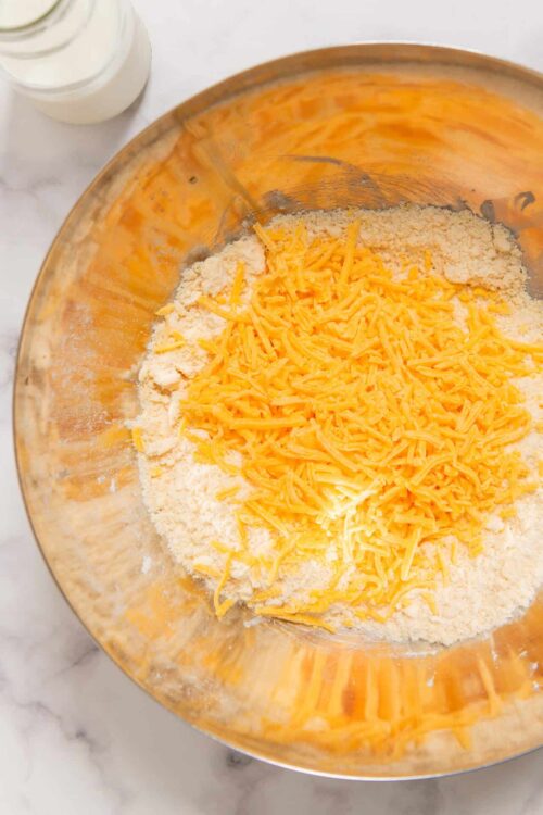 Shredded cheddar cheese and flour in mixing bowl for baking recipes.