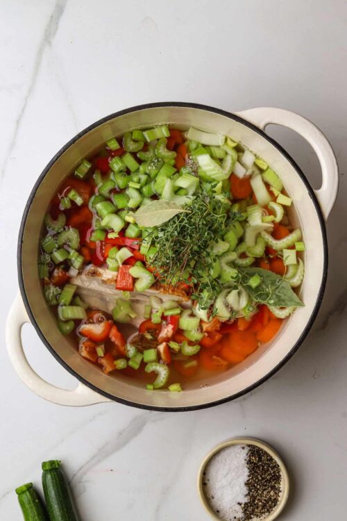 Fresh vegetable soup with celery, carrots, bell peppers, herbs, and seasoning in a pot.