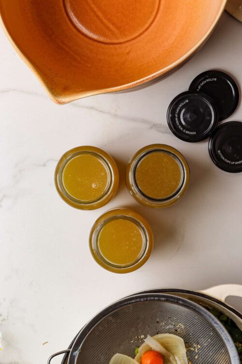Golden homemade broth in small jars for soup or cooking.