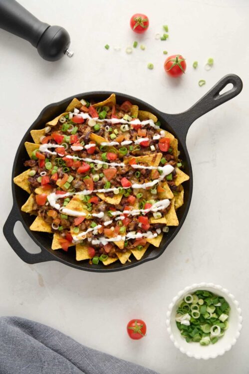 Crispy nachos with beef, tomatoes, green onions, sour cream, and salsa in a cast iron skillet.