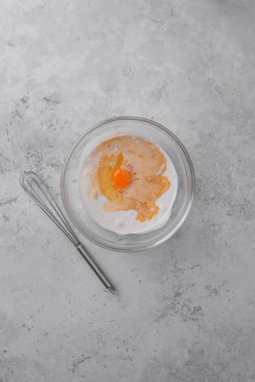 Creamy egg mixture in glass bowl with whisk on gray countertop - baking ingredients.