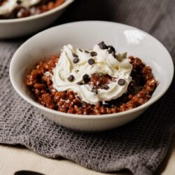 Rich chocolate pudding with whipped cream and chocolate chips in a white bowl.