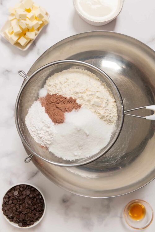 Flour, cocoa, and sugar in a sifter over a mixing bowl for baking.