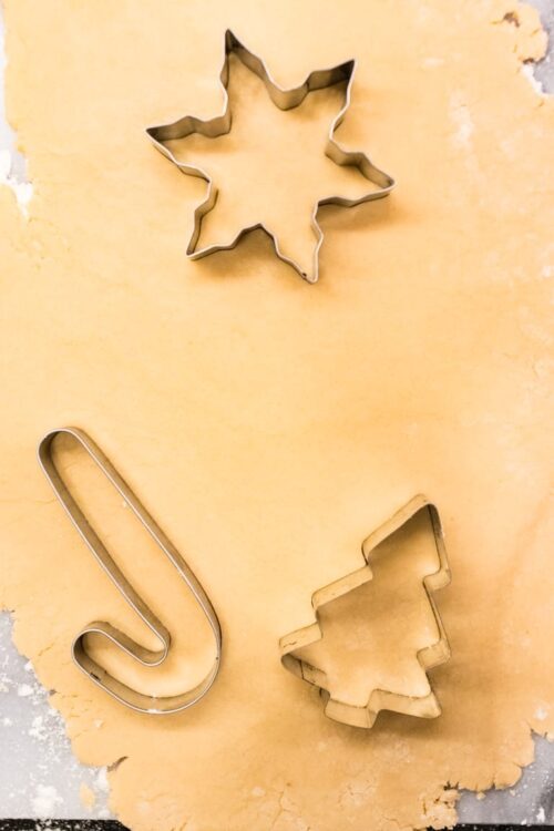 Star-shaped cookie cutter, Christmas tree cookie cutter, and candy cane cookie cutter on rolled cookie dough.