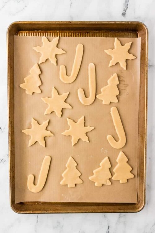 Christmas cookie dough cutouts on baking sheet, including trees, stars, and candy canes, ready for baking.