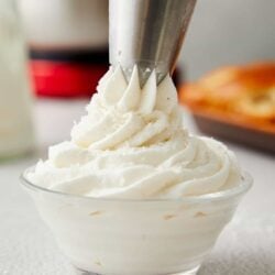Fluffy homemade whipped cream being piped into a glass bowl with a pastry bag.