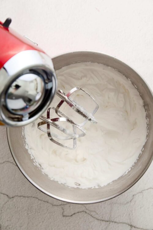 Whipped cream in a mixing bowl with a hand mixer; baking and dessert recipes.