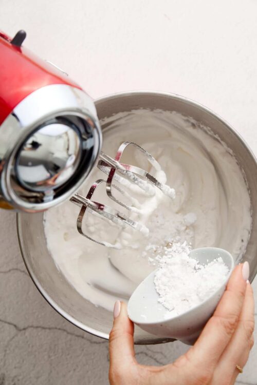 Fluffy whipped cream being made with a hand mixer in a metal bowl.