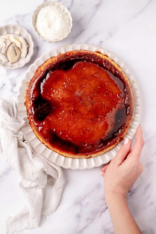 Butter tart with glossy caramel glaze on white plate with baking ingredients nearby.
