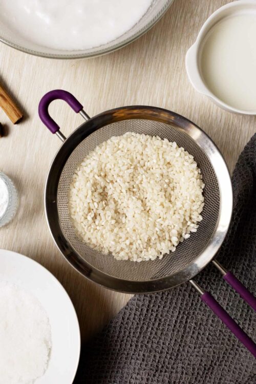 Cooked white rice in a mesh strainer on a wooden surface.