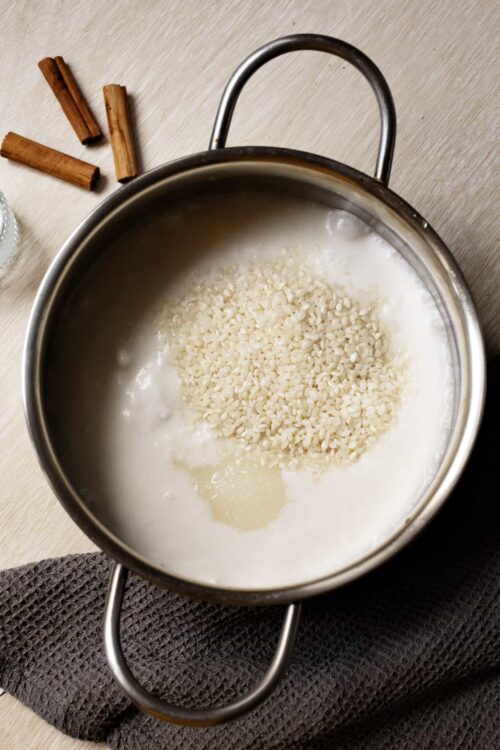 Creamy coconut rice cooking in a stainless steel pot on a wooden surface.