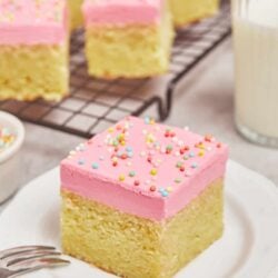 Buttered vanilla cake with pink frosting and colorful sprinkles, close-up of a bakery-style dessert.