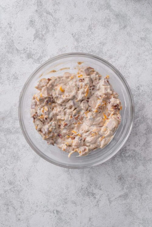 Creamy chicken salad with shredded cheese and fresh ingredients in a glass bowl.