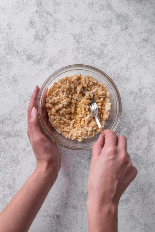 Crumb mixture in glass bowl with hands mixing, baking ingredients, preparing dessert.