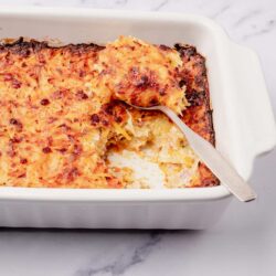 Baked cheesy potatoes casserole in white dish with a serving spoon.