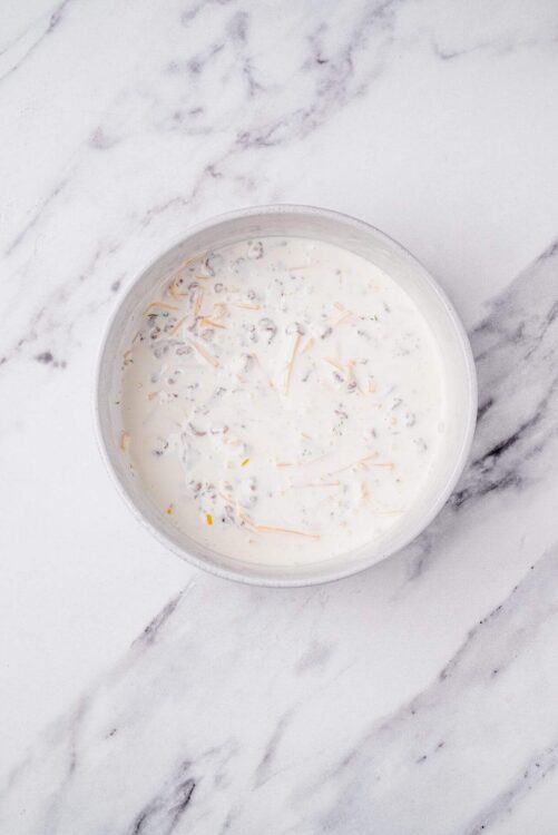 Whipped cream with shredded cheese in a bowl on marble surface, ideal for dessert toppings or savory dishes.