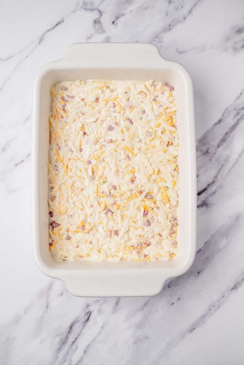 Creamy cheeseburger casserole ready to bake, topped with shredded cheese in a white baking dish.