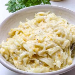 Creamy homemade macaroni and cheese in a white bowl with fresh parsley and a wooden pepper mill in the background.