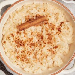 Buttered rice pudding topped with cinnamon and a cinnamon stick, served in a white ceramic dish.