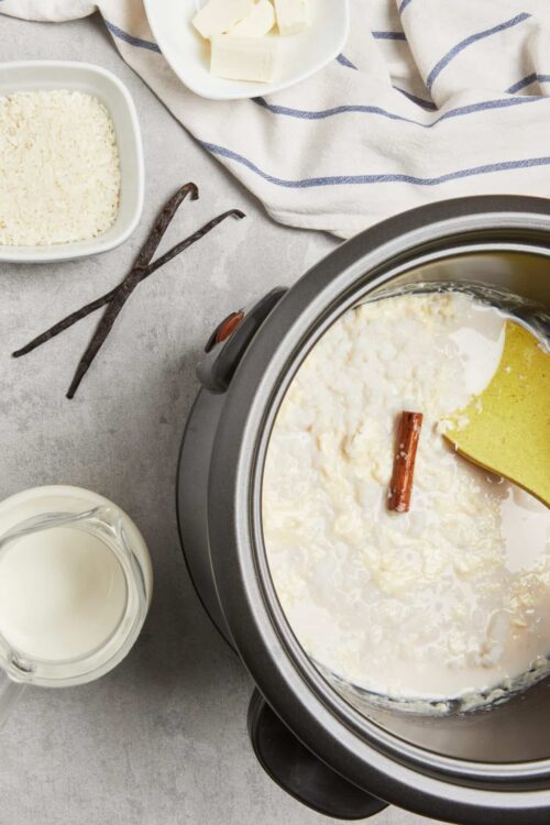 Cream cheese in slow cooker with cinnamon stick and milk for homemade cheesy recipes.