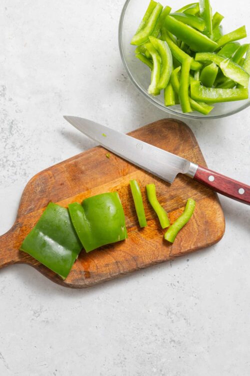 Fresh green bell pepper being sliced on a wooden cutting board for healthy cooking.