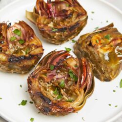 Baked artichokes stuffed with herbs and cheese on a white plate.