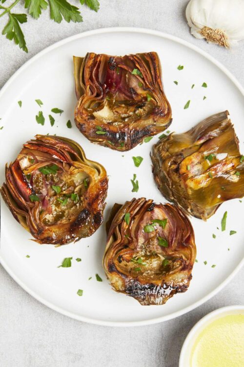 Roasted artichoke hearts garnished with fresh herbs on white plate.