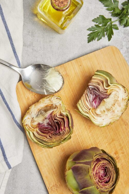 Fresh roasted artichoke hearts on a wooden cutting board with olive oil and herbs, healthy vegetables for cooking and eating.