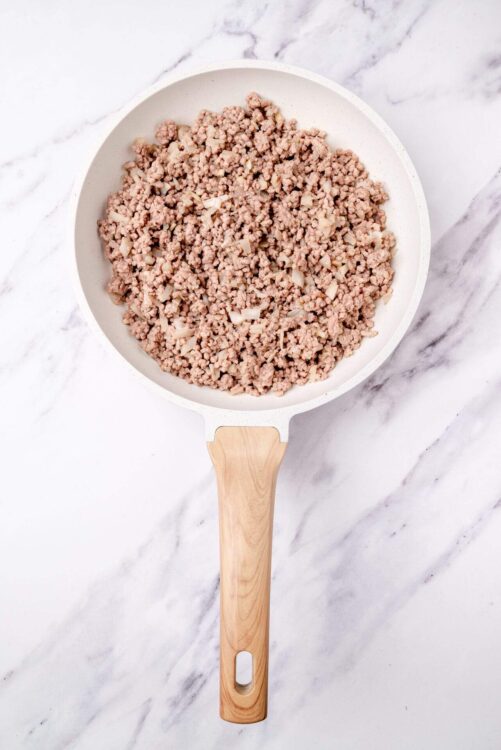 Ground turkey in a white skillet on marble background, ready for cooking.