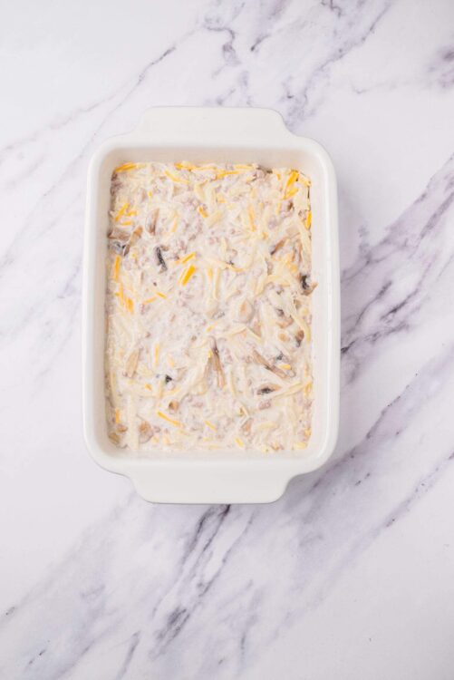 Creamy chicken and mushroom casserole with shredded cheese in a white baking dish.