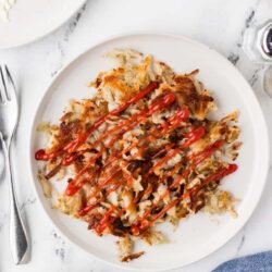 Crispy hash browns with ketchup drizzle on a white plate.
