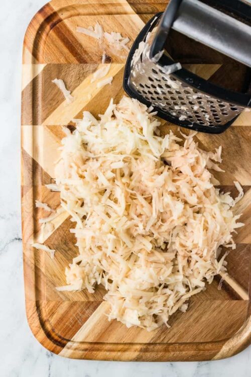Finely shredded mozzarella cheese on wooden cutting board with cheese grater.
