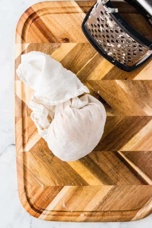 Soft cheese cloth for cheese making on wooden cutting board with cheese grater, kitchen tools for cheese preparation, Baked Bree.