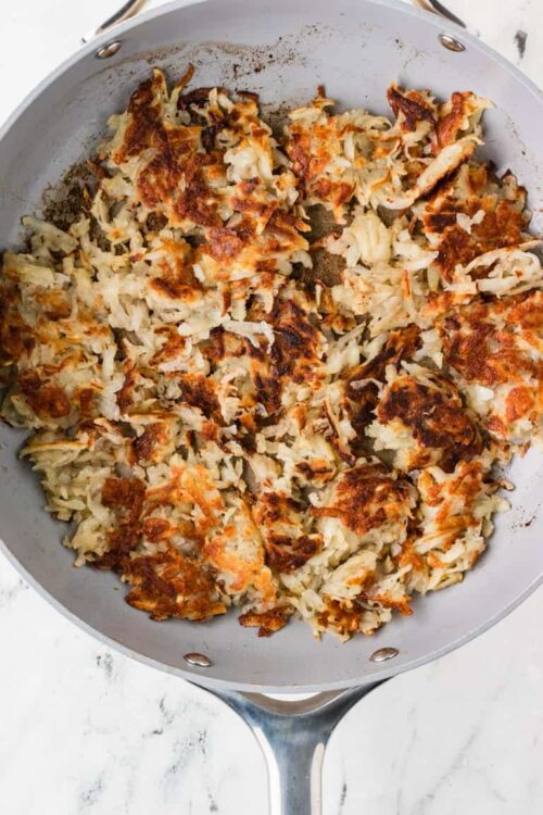 Shredded cooked chicken and crispy hash browns in a skillet, ready for a breakfast casserole.