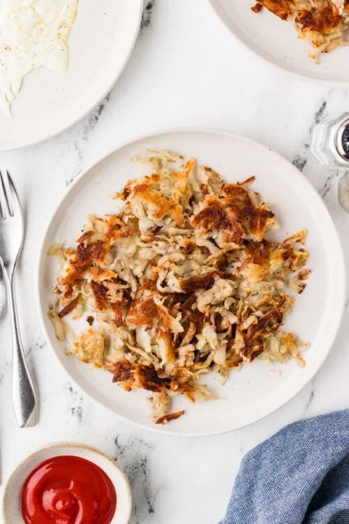 Cooked shredded chicken casserole on white plate with crispy golden topping and side dishes.