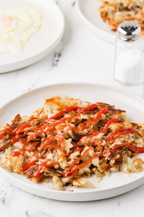 Crispy hash brown casserole with ketchup drizzled on top, served on a white plate.