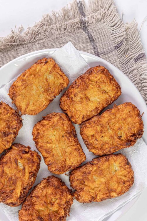 Crispy homemade fried potato cakes on white paper towel.