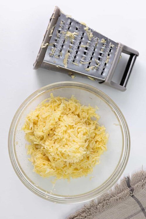 Shredded cheese in a glass bowl with a cheese grater on white background.