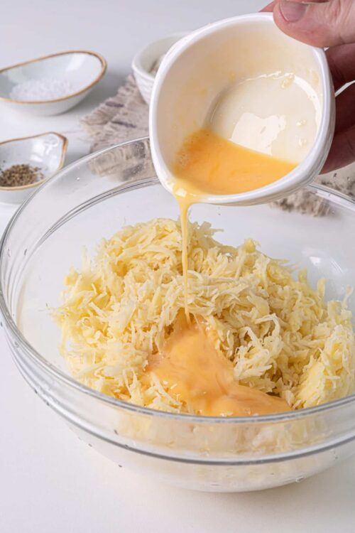 Cream being poured into shredded cheese in glass mixing bowl for cheese dip recipe.