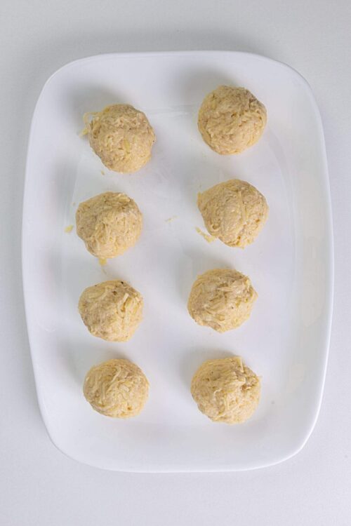 Dough balls for cheese ball appetizer on white plate, ready to be rolled and served.